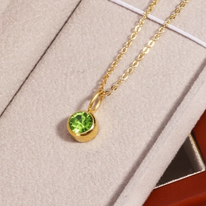 Close-up of a gold necklace with round green birthstone pendant in a jewelry box