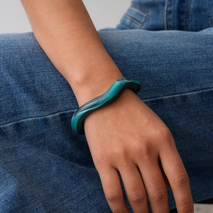 Detail of a wavy green acrylic cuff bracelet worn against blue denim fabric backdrop