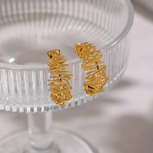 Detailed close-up of golden irregular wire-wrapped hoop earrings on a glass rim