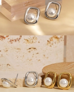 Detailed view of square gold and silver earrings with large white pearls on stone background