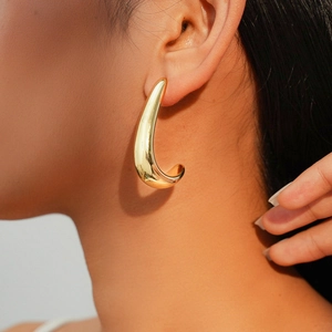 Gros plan d'un mannequin portant de grandes boucles d'oreilles goutte d'eau dorées polies