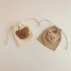 Detail view of cream and khaki corduroy drawstring pouches with plush bear decorations