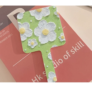 Detail of green handheld makeup mirror with embossed white flower and yellow center