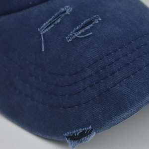 Close-up of distressed cotton baseball cap showing washed fabric texture and frayed details