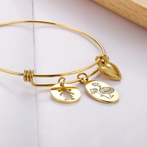 Detail of adjustable gold bangle with heart, girl, and daisy charms on a clean background