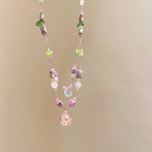 Detail of beaded necklace with glass flowers and colorful square beads on pink strand