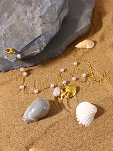 Detail of beach-style gold seashell and starfish necklace with baroque pearls on sand