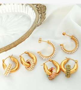 Detail of gold hoop earrings with pearls and colorful zircons on white silk background