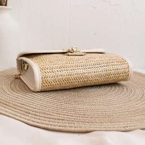 Straw woven crossbody bag with metal clasp and chain strap on minimalist background