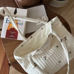 Detail of white quilted tote bag with orange embroidery and internal storage pocket
