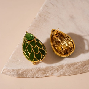 Gros plan sur boucles d'oreilles en émail vert avec motif écailles dorées sur pierre
