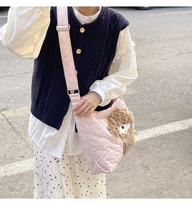 Pink quilted crossbody bag with heart pattern and brown teddy bear charm on blue outfit