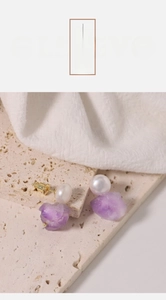 Makro-Detail von asymmetrischen Amethyst- und Süßwasserperlen-Ohrsteckern auf Stein