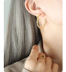 Close-up of golden bamboo texture hoop earrings and emerald square gemstone ring on model