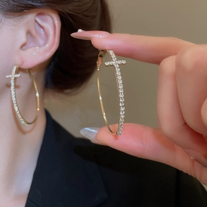 Gros plan d'une grande créole dorée avec strass et pendentif croix sur un mannequin