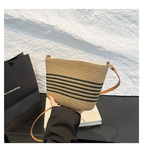 Detail of woven straw bucket bag with black stripes and brown leather strap