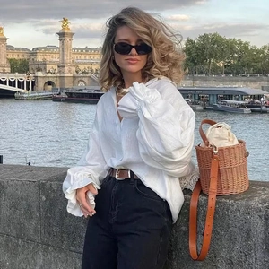 Outdoor street style view of a long-sleeve linen shirt paired with a straw bucket bag