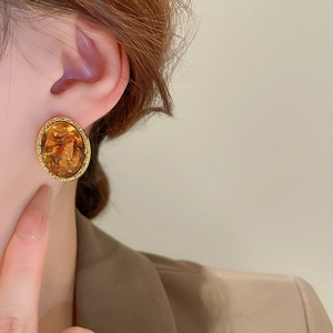 Close-up of geometric gold-framed amber resin earrings worn by a model in profile