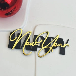 Detail of Happy New Year acrylic cake topper in gold and black with red ornament