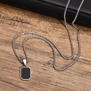 Detail of a minimalist black rectangular pendant on a silver box chain over a wood surface