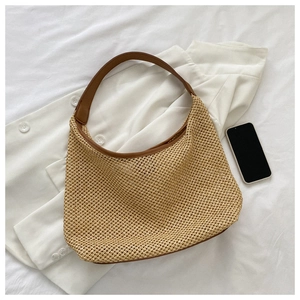 Detail view of beige woven straw tote bag with brown leather straps on white bedding
