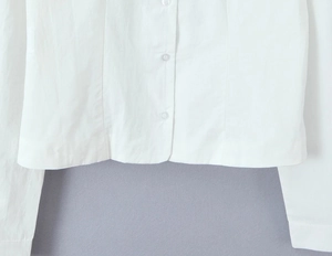 Close-up of white blouse hem showing stitching and transparent resin buttons details