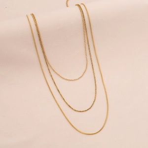 Detailed view of triple-layered golden necklace with sleek snake chain on beige fabric