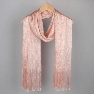 Rose gold metallic shawl with fringe tassels hanging on a wooden hanger against a grey wall