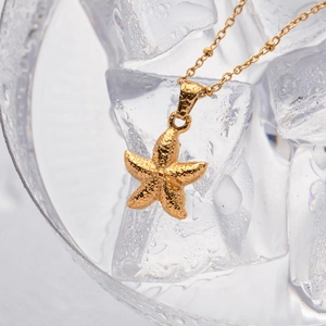 Macro view of gold starfish pendant with bead chain and water drops on ice cubes