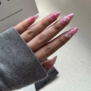 Macro view of long almond press-on nails with 3D floral accents and pink gradient