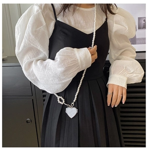Detail der Perlenkette und des weißen Herzanhängers auf einem schwarz-weißen Faltenkleid
