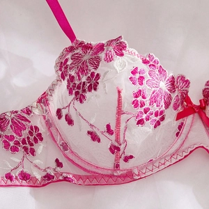 Detail of floral embroidery on white mesh bra with pink satin straps and bow