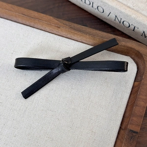 Detailed close-up of a black leather bow hair clip on a minimalist wooden tray
