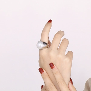 Détail d'une bague large en acier inoxydable ornée d'une grande perle sur un doigt