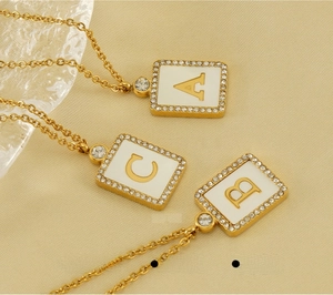 Macro detail of gold square alphabet pendants A B C with white shell and pavé crystals