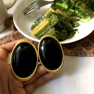 Close-up of vintage oval black earrings with gold frame in a lifestyle cafe setting