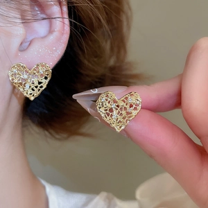 Detailed view of heart shaped gold metal stud earrings with lace cutouts and crystals