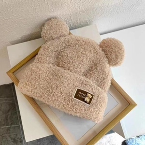 Detailed view of beige plush knit hat with bear ears and small golden bear metal clasp