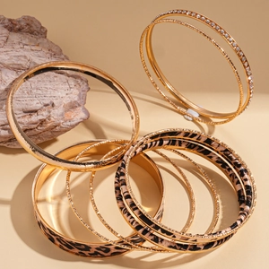 Dettaglio di set di bracciali dorati multistrato con stampa leopardata e strass