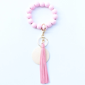 Porte-clés bracelet en perles de bois roses avec pompon en cuir et anneau doré sur blanc