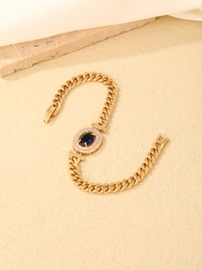 Detail of a gold Cuban link bracelet featuring a blue oval gemstone with zircon pave