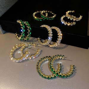 Detailed view of gold C-shape earrings with emerald green and clear zircon stones