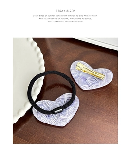 Detail showing a purple woven texture heart hair clip and elastic tie on wood surface