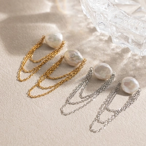 Dettaglio di orecchini con perle barocche e nappe in finitura oro e argento su base opaca