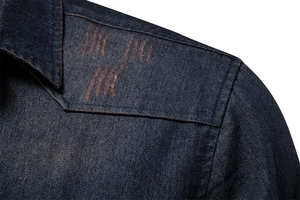 Close-up of deep blue denim shirt featuring decorative red embroidery on shoulder seam