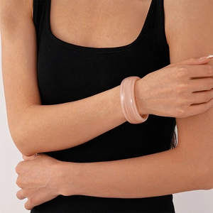 Detail of a pink acrylic chunky bangle on a model's wrist with a black minimalist outfit