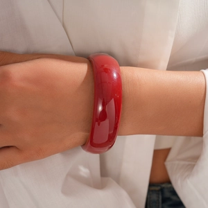 Close-up of a wide glossy red resin bangle worn over a white shirt sleeve