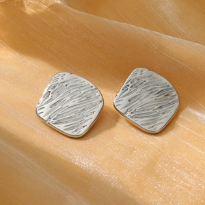 Brushed silver wrinkled texture square earrings on orange silk fabric background