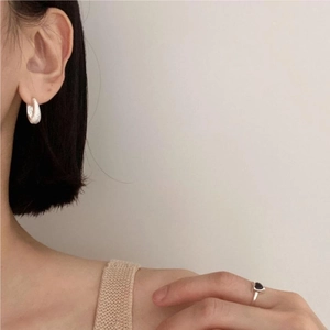 Detail view of silver textured hoop earring and black heart ring on a model