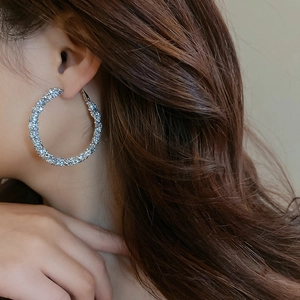 Close-up of woman wearing large silver geometric hoop earrings with sparkly diamond texture